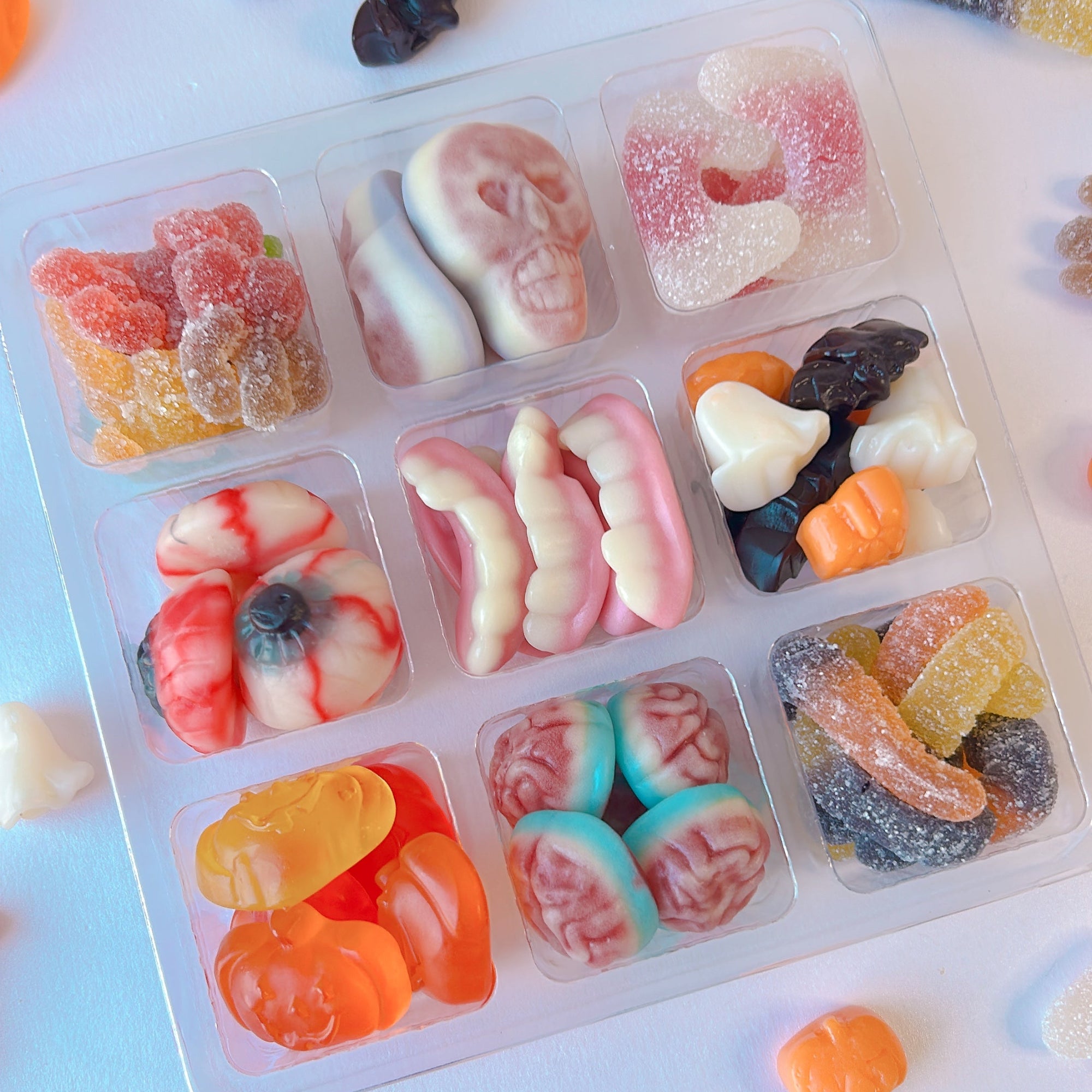 A clear plastic candy organizer tray filled with assorted Halloween-themed gummy candies, surrounded by loose gummy sweets