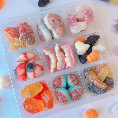 A clear plastic candy organizer tray filled with assorted Halloween-themed gummy candies, surrounded by loose gummy sweets