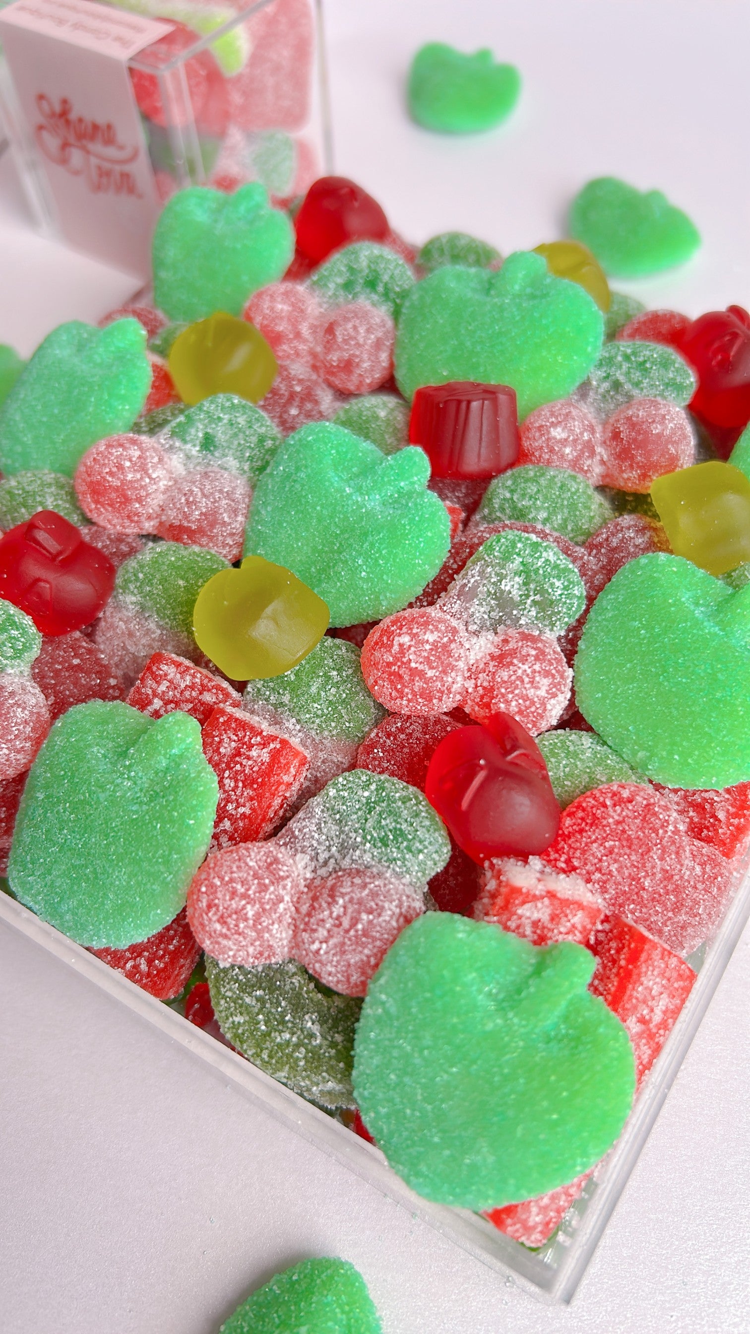 Assorted gummy candies including green, red, shapes in an acrylic candy tray