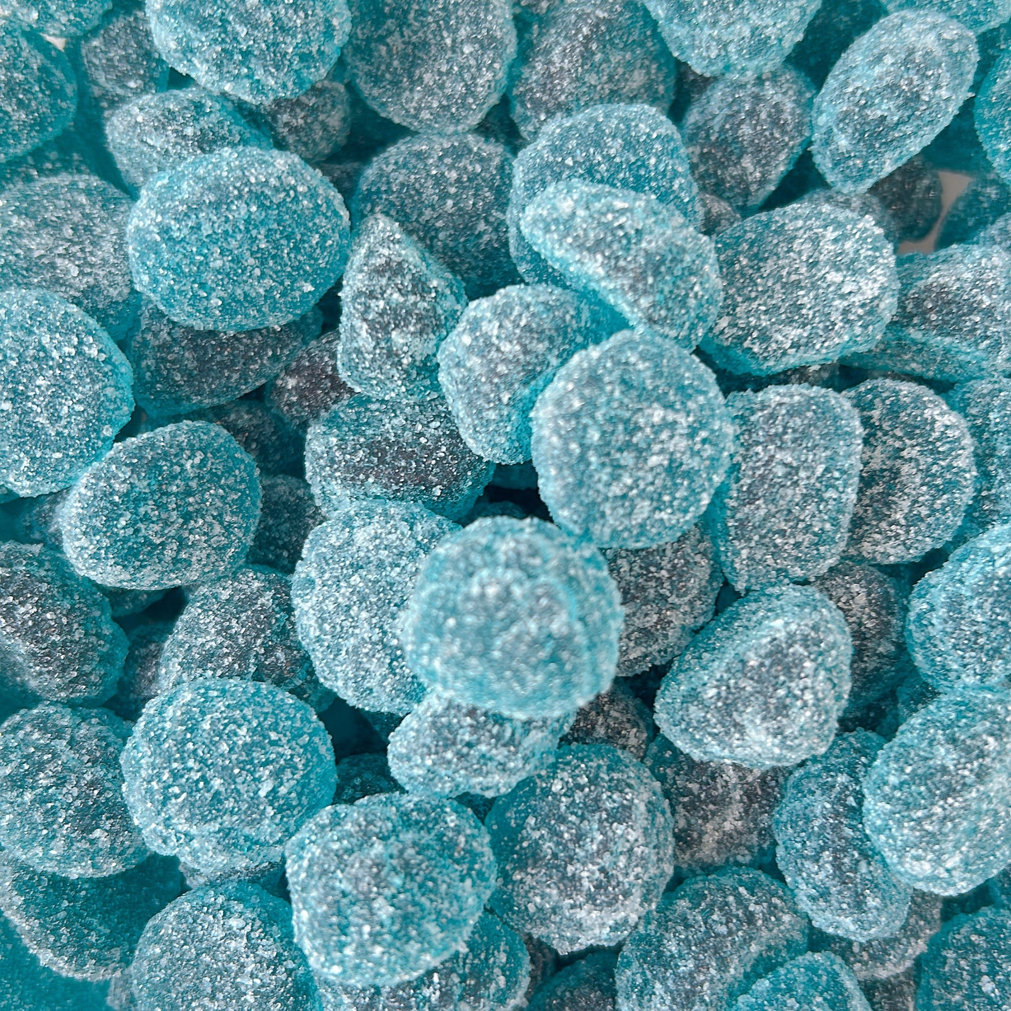 A pile of round, sugar-coated gumdrops in a bright turquoise blue color.