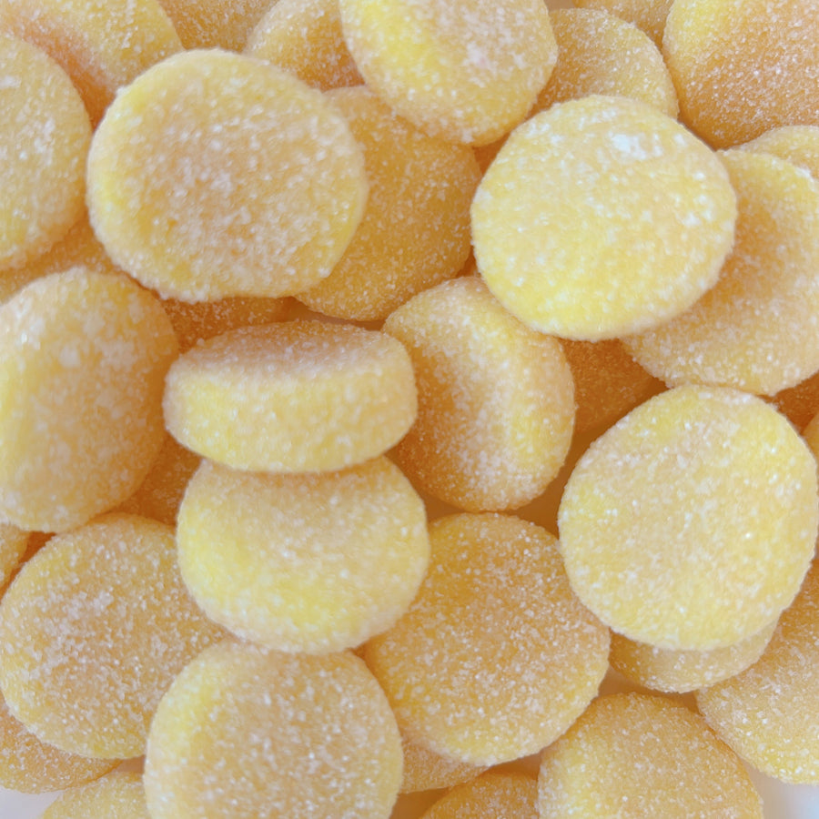Pile of yellow sour gummy candy in round shape in the flavour of pineapple and orange