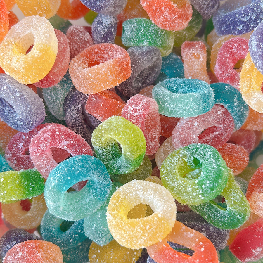 A close-up pile of colorful sugar-coated ring-shaped gummy candies in many shades including orange, yellow, green, blue, purple, and pink.