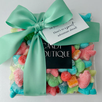 A clear gift bag filled with colorful candy, tied with a large mint green satin bow and a small white tag that reads 'Candy Boutique'.